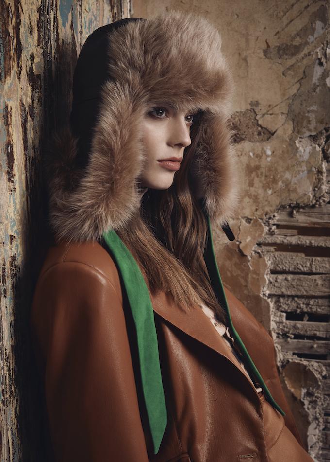 Chestnut brown shearling aviator hat with green suede straps on model