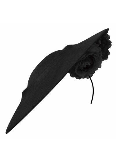 The black Gwen hat is a mid-size straw disc hat, worn asymmetrically with a trio of silk flowers under the brim